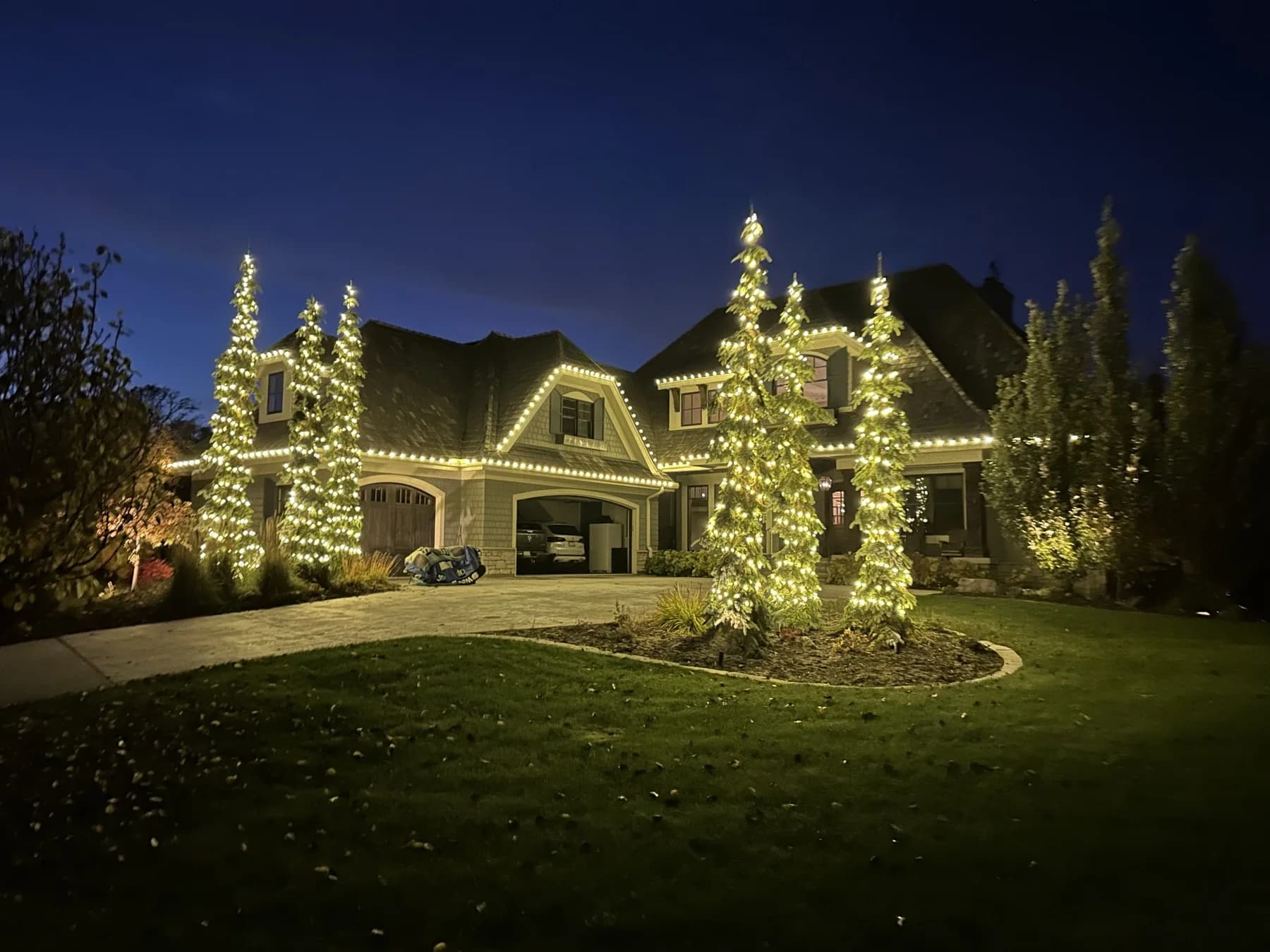 Luxury Twin Cities home with warm white Christmas lights on tall cypress trees — FCR Cleaning holiday lighting installation