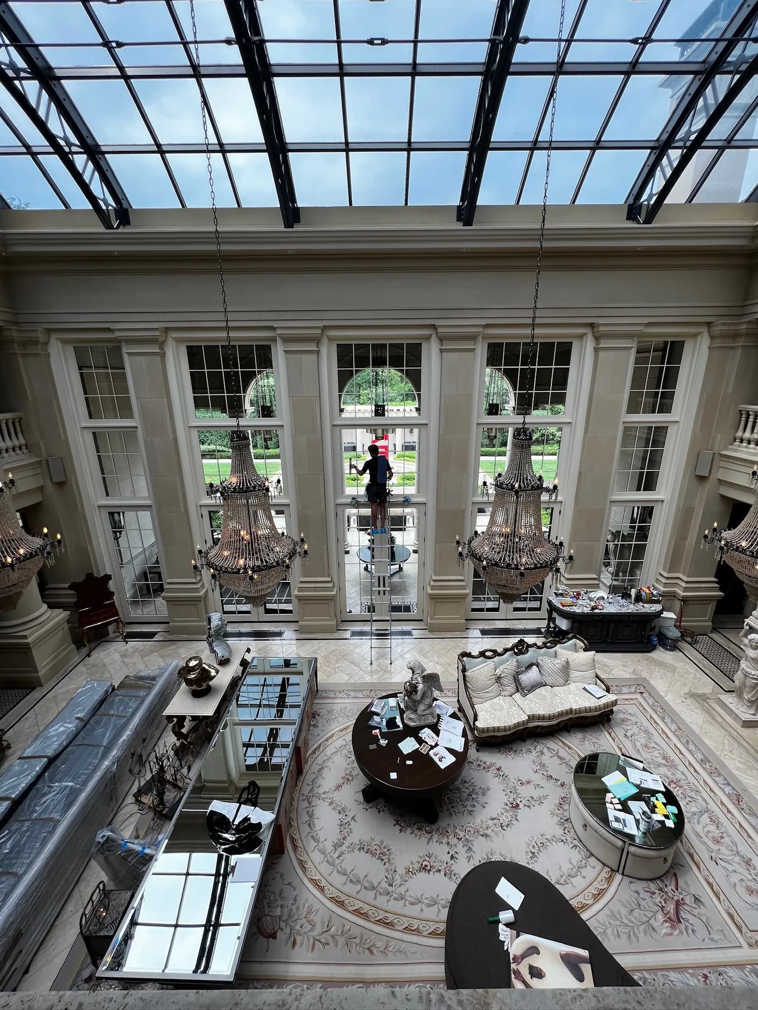 Overhead view inside a Twin Cities luxury estate — FCR Cleaning crew visible through soaring windows with twin chandeliers